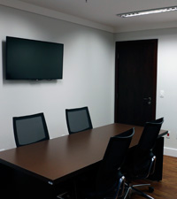 Ambiente de reuni&otilde;es na Diretoria-Geral com televis&atilde;o na parede e porta ao fundo
